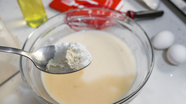 Kitchen spoon holding flour over a bowl containing white liquid