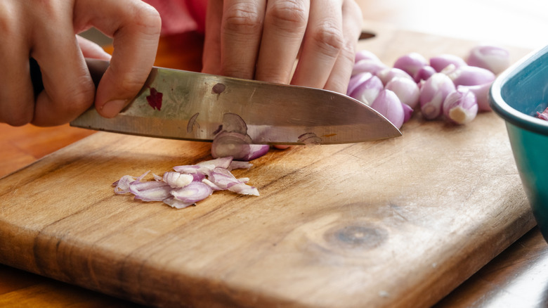 Person chopping shallot on a cutting board while holding their hands in the proper grip