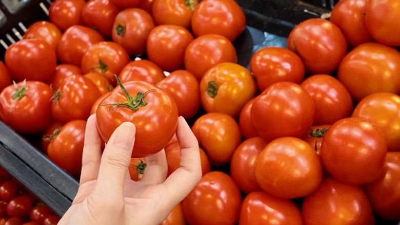 A hand holds a tomato in a grocery store