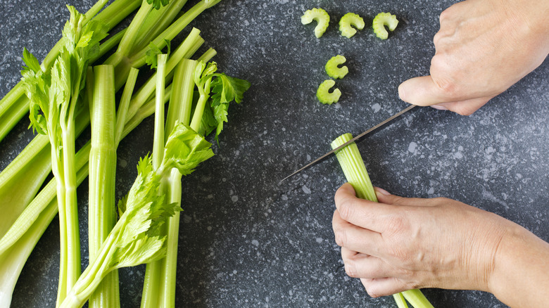Hands chopping trimmed celery on cutting board