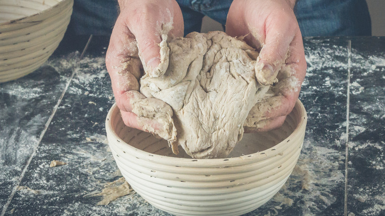 Holding proofed bread dough over a bowl 