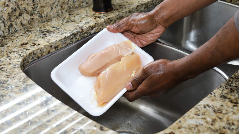 Hands holding chicken in sink
