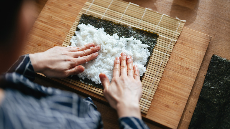 a person placing sushi rice on seaweed