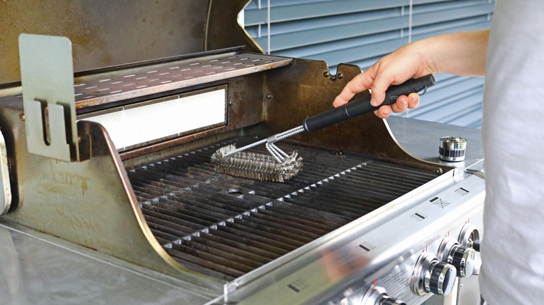 A person cleaning a grill with a wire grill brush on the patio