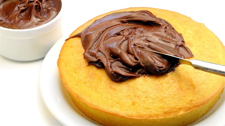 Chocolate frosting spread on yellow cake
