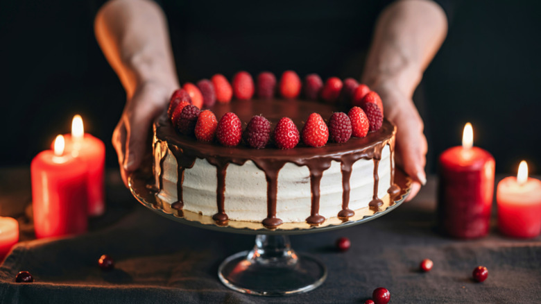 Chocolate and strawberry cake on a cake stand being held by two hands and flagged by red candles