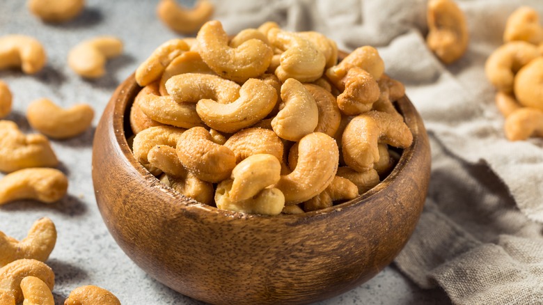 Salted cashews in a wooden bowl surrounded by cashews