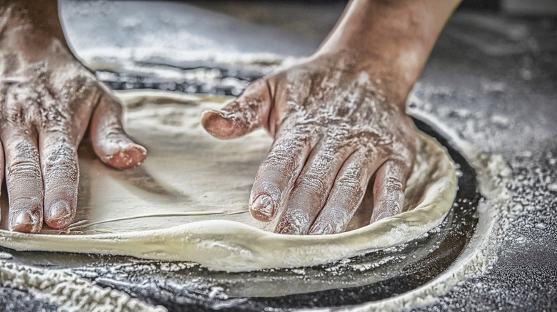 A close-up on floured hands spreading pizza dough