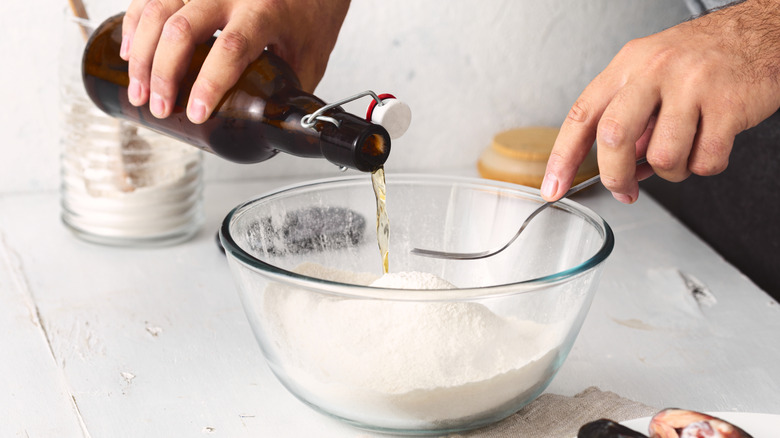 A close-up on hands adding beer to flour in a Pyrex bowl to make beer batter