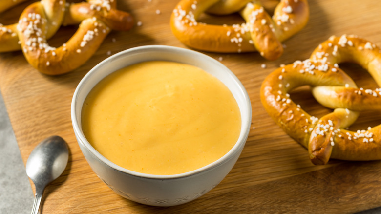 A bowl of beer cheese dip on a platter with fresh pretzels