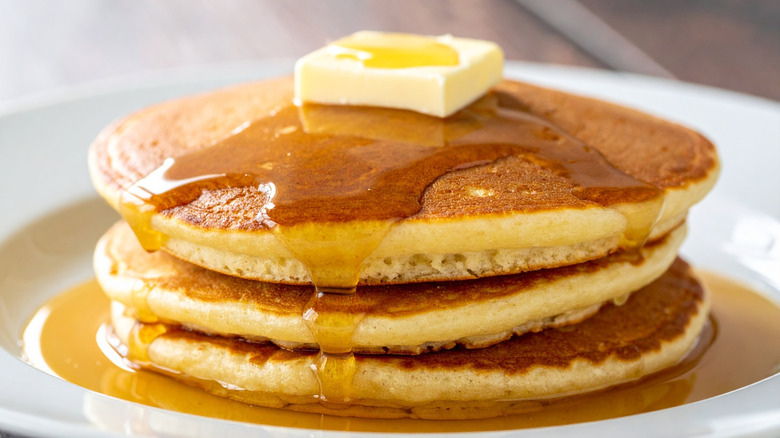 A close-up on a stack of pancakes topped with butter and syrup