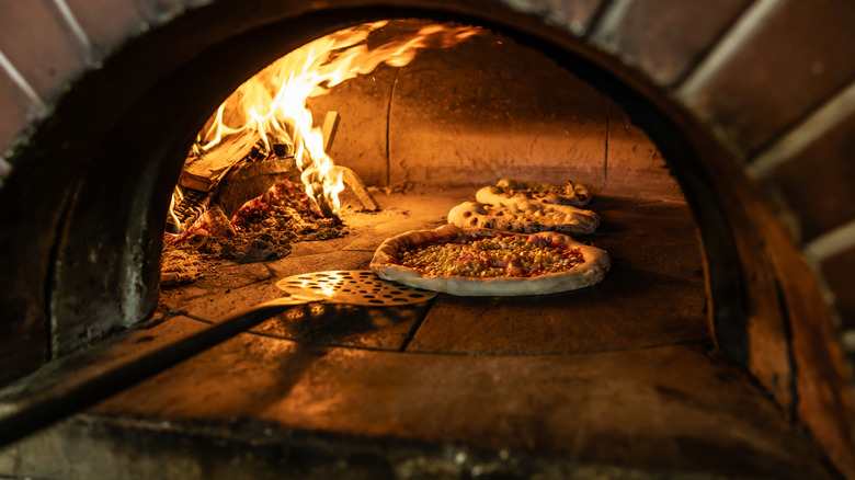 A pizza is being turned in a brick pizza oven with fire on the left side