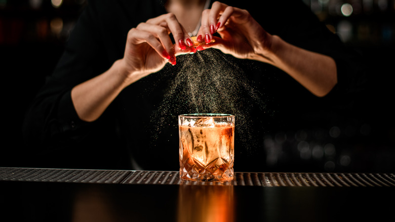 Bartender squeezing orange into Old Fashioned cocktail