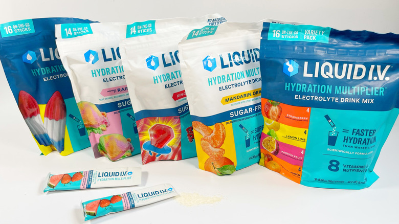 Several bags of different kinds of Liquid I.V. With one stick spilling powder on a white background