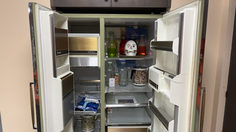The open refrigerator full with various bottles and a white fake skull