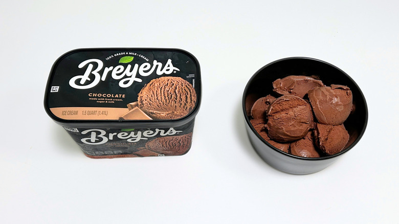 A tub of Breyers Chocolate Ice Cream next to a black bowl of ice cream