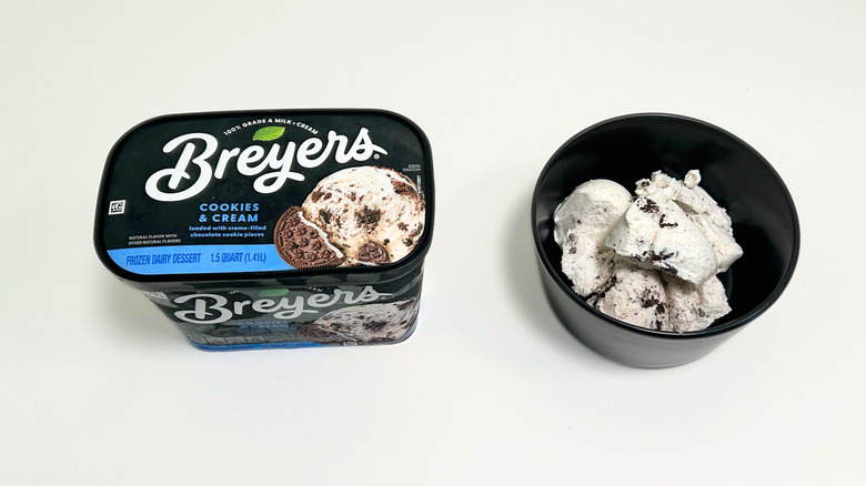 A tub of Breyers Cookies and Cream Ice Cream next to a black bowl of ice cream