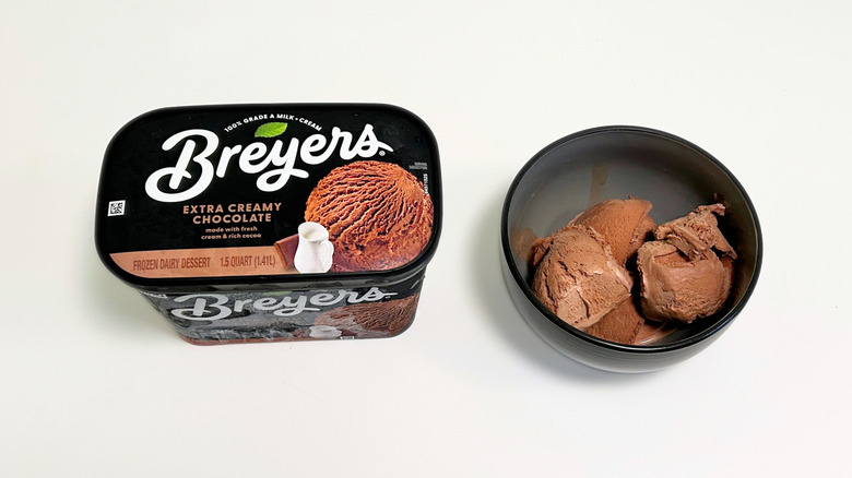 A tub of Breyers Extra Creamy Chocolate Ice Cream next to a black bowl of ice cream
