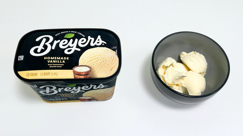 A tub of Breyers Homemade Vanilla Ice Cream next to a black bowl of ice cream