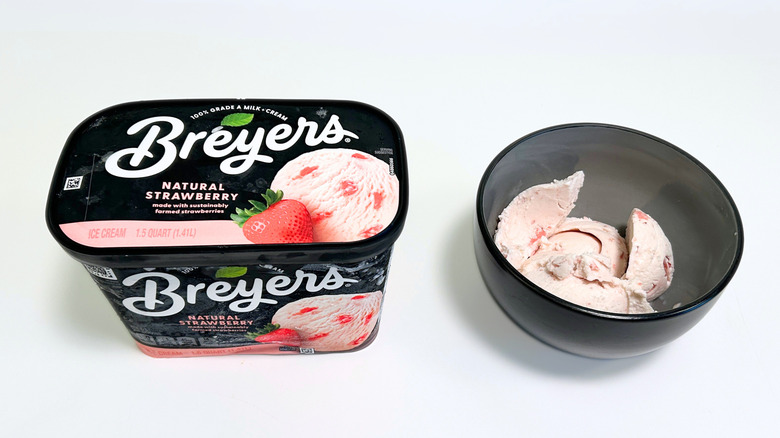 A tub of Breyers Natural Strawberry Ice Cream next to a black bowl of ice cream