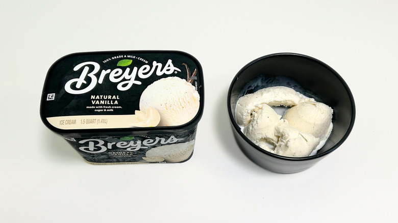 A tub of Breyers Natural Vanilla Ice Cream next to a black bowl of ice cream