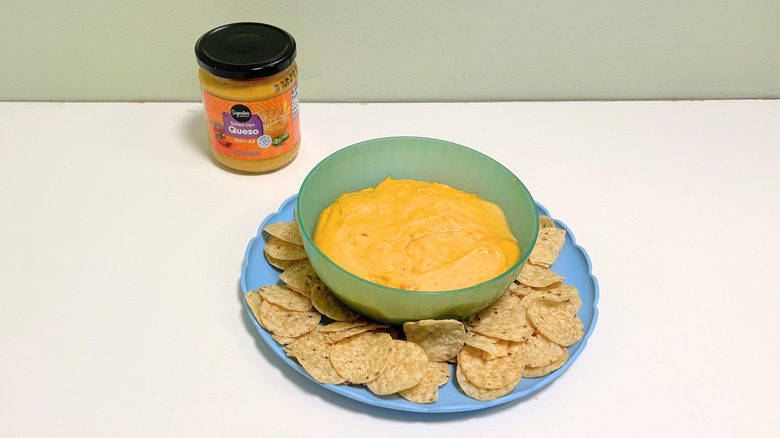 A bowl of queso surrounded by tortilla chips next to a jar of Signature Select Salsa Con Queso