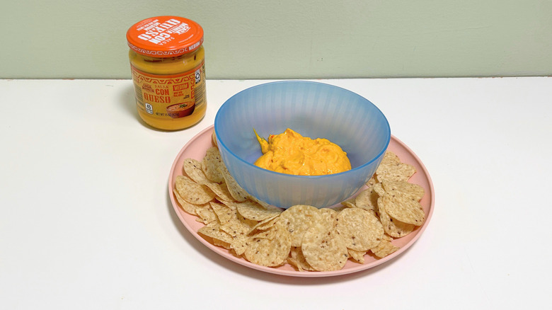 A bowl of queso surrounded by tortilla chips next to a jar of Casa Mamita Salsa Con Queso