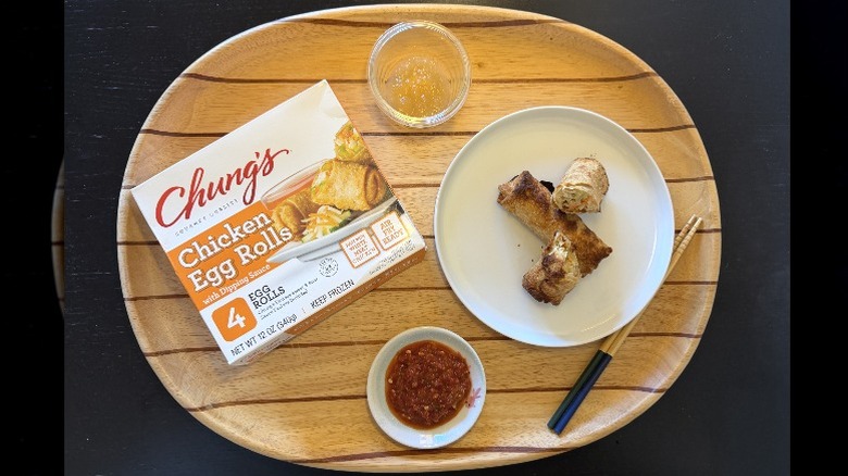 Chung's White Meat Chicken Egg Rolls on a wooden tray next to their box and a dish of sambal