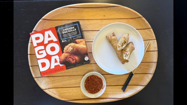 Pagoda Frozen Crunchy Crispy Chicken Egg Rolls on a wooden tray next to their box and a dish of sambal