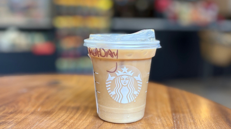 A light brown cup of a Starbucks drink on a wood table with a blurry background