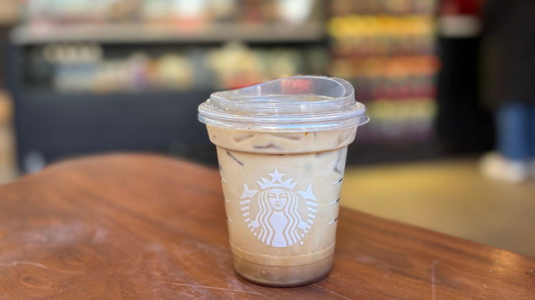 A light brown cup of a Starbucks drink on a wood table with a blurry background