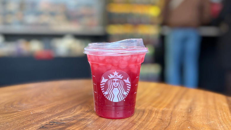 A red cup of a Starbucks drink on a wood table with a blurry background