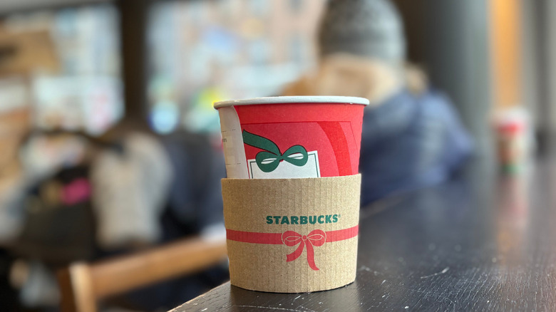 A red cup of a Starbucks drink on a black wood table with a blurry background