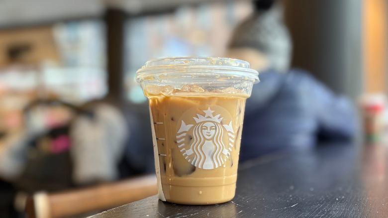 A beige cup of a Starbucks drink on a black wood table with a blurry background