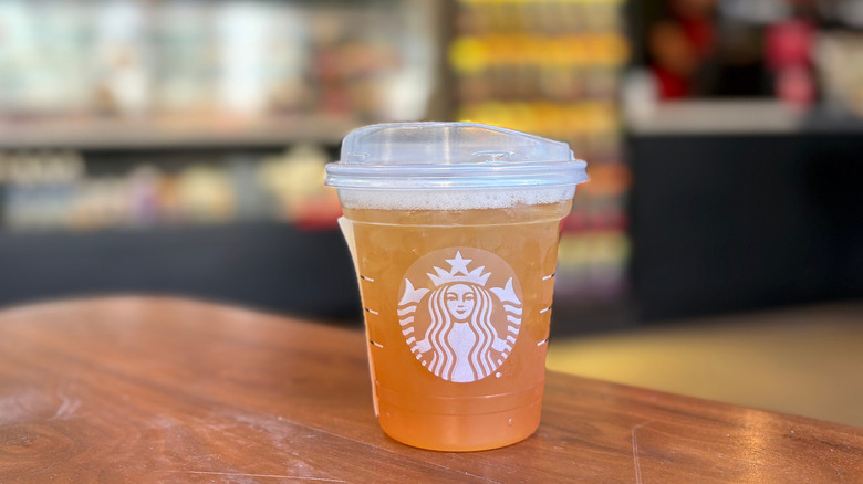 A orange cup of a Starbucks drink on a wood table with a blurry background
