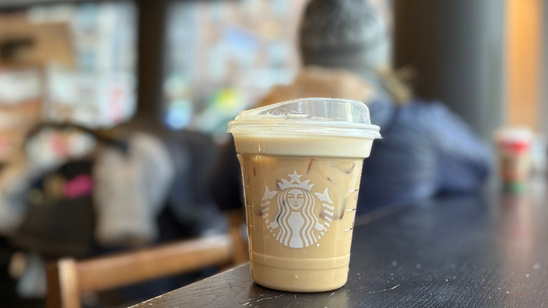 A clear cup of a Starbucks drink on a black wood table with a blurry background