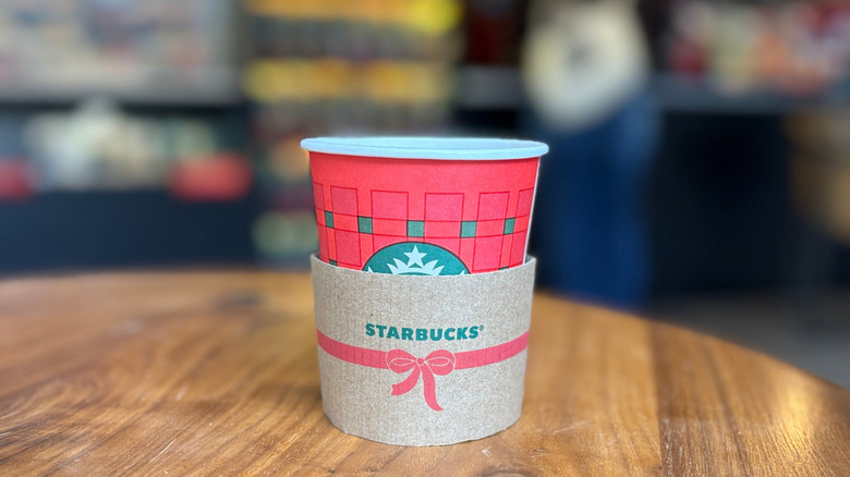 A red cup of a Starbucks drink on a wood table with a blurry background