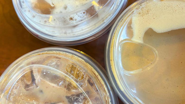The zoomed in tops of three starbucks coffee drinks on a wood table