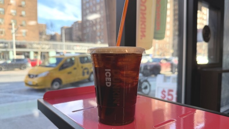 A Dunkin' Blueberry and Vanilla Iced Coffee in front of a window