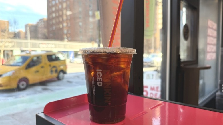 A Dunkin' Hazelnut Sugar-Free Vanilla Iced Coffee in front of a window