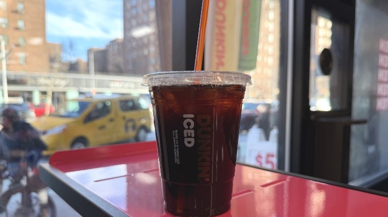 A Dunkin' Iced Americano in front of a window