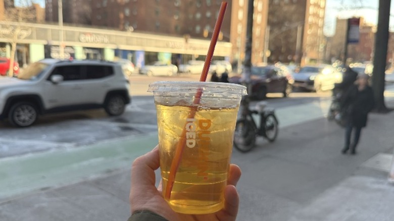 A hand holding a Dunkin' Iced Green Tea