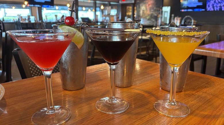 Three Applebees cocktails in front of shakers on wooden table
