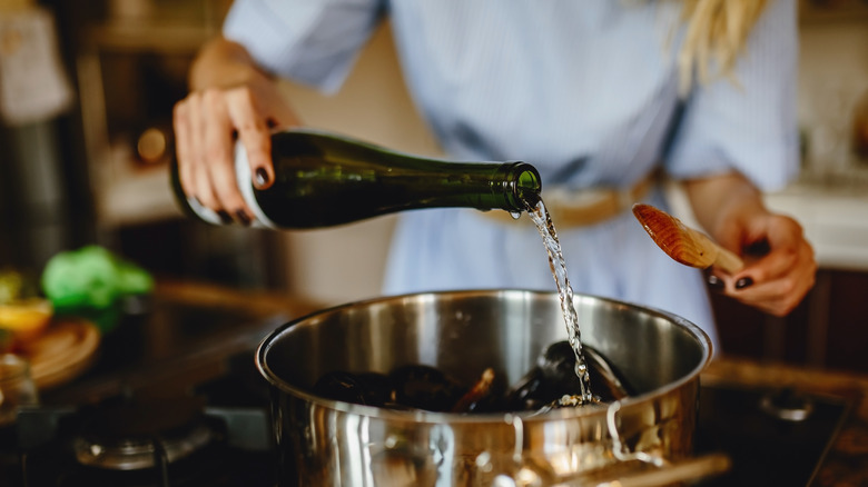 person pouring white wine in pot of mussels
