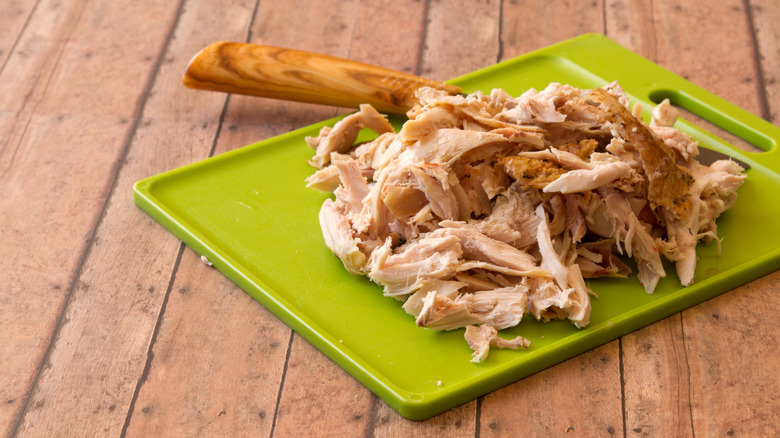 Shredded rotisserie chicken on a green cutting board on top of a wooden slat tabletop.
