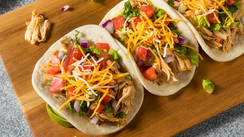 three chicken tacos on a wooden cutting board
