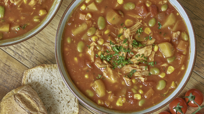 Homemade Brunswick stew with shredded chicken, beans, potatoes, corn and tomato and BBQ sauces, served in a blue bowl on a wooden table.