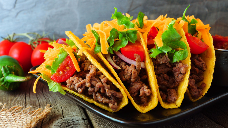 Three hardshell tacos with ground beef, cheddar cheese, tomato, lettuce, and onions