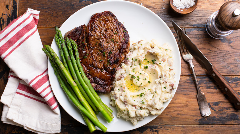 A steak dinner with mashed potatoes and asparagus on a wooden table