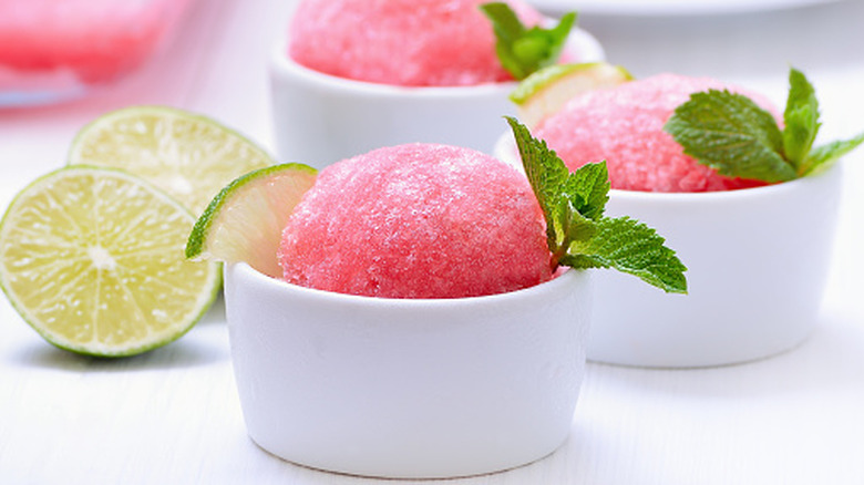 Small white bowls of watermelon granita garnished with lime slices and fresh mint